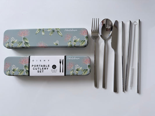 A flat-lay view of a portable cutlery set on a white background, featuring stainless steel utensils (spoon, fork, knife, straws) and their matching floral-patterned storage cases with a central paper label.