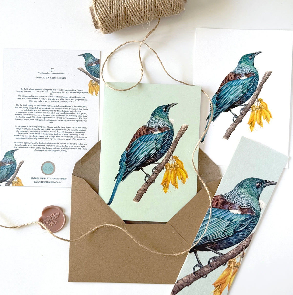 A styled flat-lay of a bird-themed stationery set featuring a watercolor illustration of a blue-green bird perched on a branch with yellow flowers. The set includes a light green greeting card, a kraft paper envelope, a printed invitation card with text, a bookmark, and twine with a wax seal, arranged on a white background.
