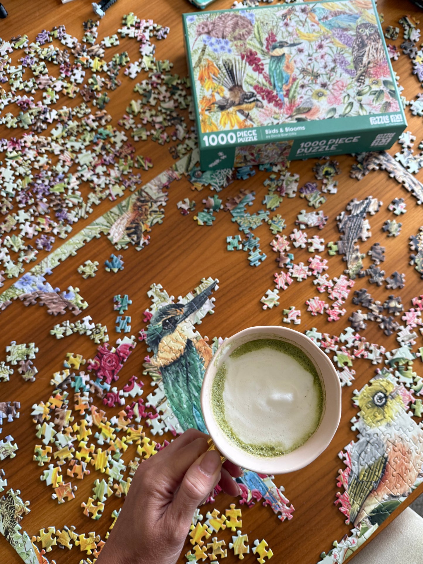 Puzzle pieces on a table with a cup of tea and a box of puzzles.