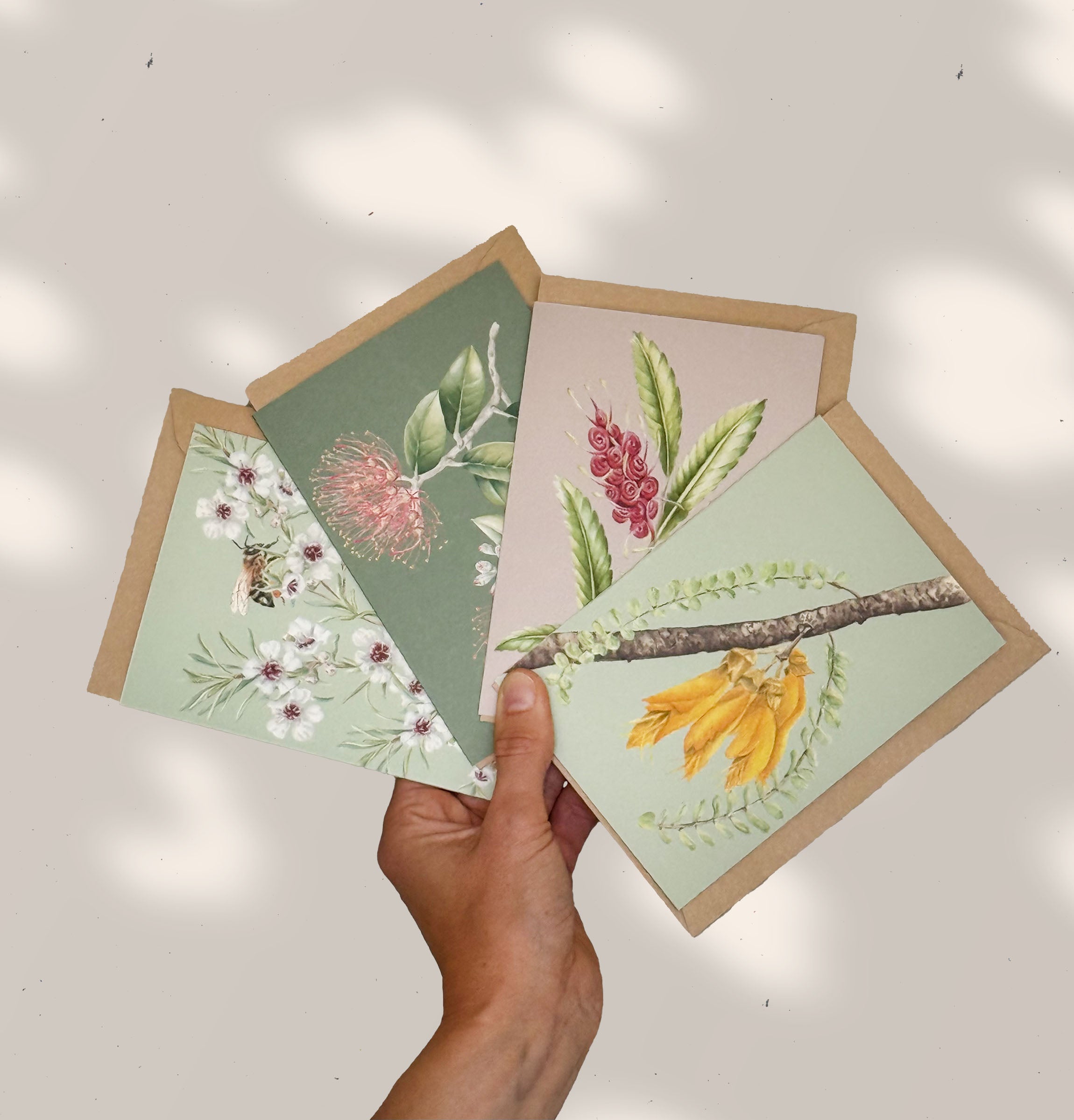 Hand holding four botanical-themed greeting cards with floral and nature designs on a light background.